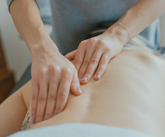 Frau, der der Rücken massiert wird, sie liegt mit dem Gesicht nach unten auf einer Massageliege