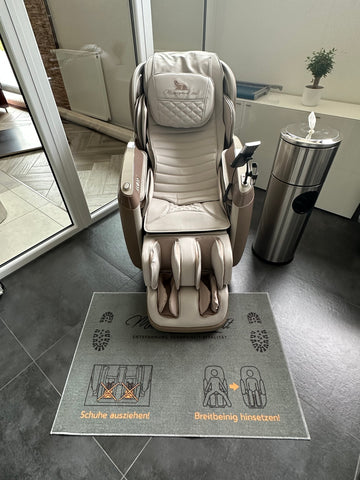 Hinweis-Fußteppich „Schuhe ausziehen“ vor einem Massagesessel