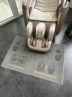 
Hinweis-Fußteppich „Schuhe ausziehen“ vor einem Massagesessel